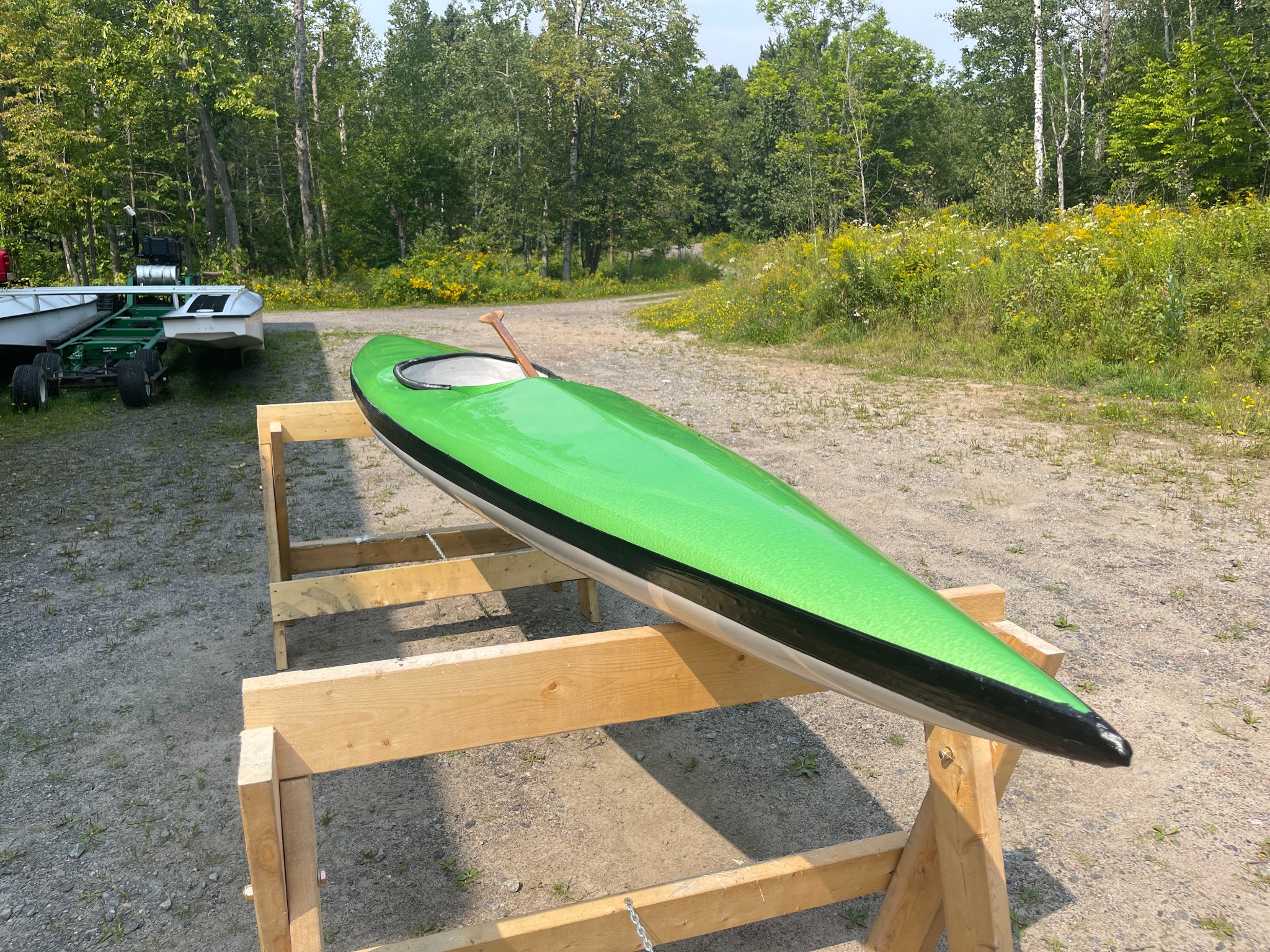 Completed green kayak resting on wooden stands outdoors